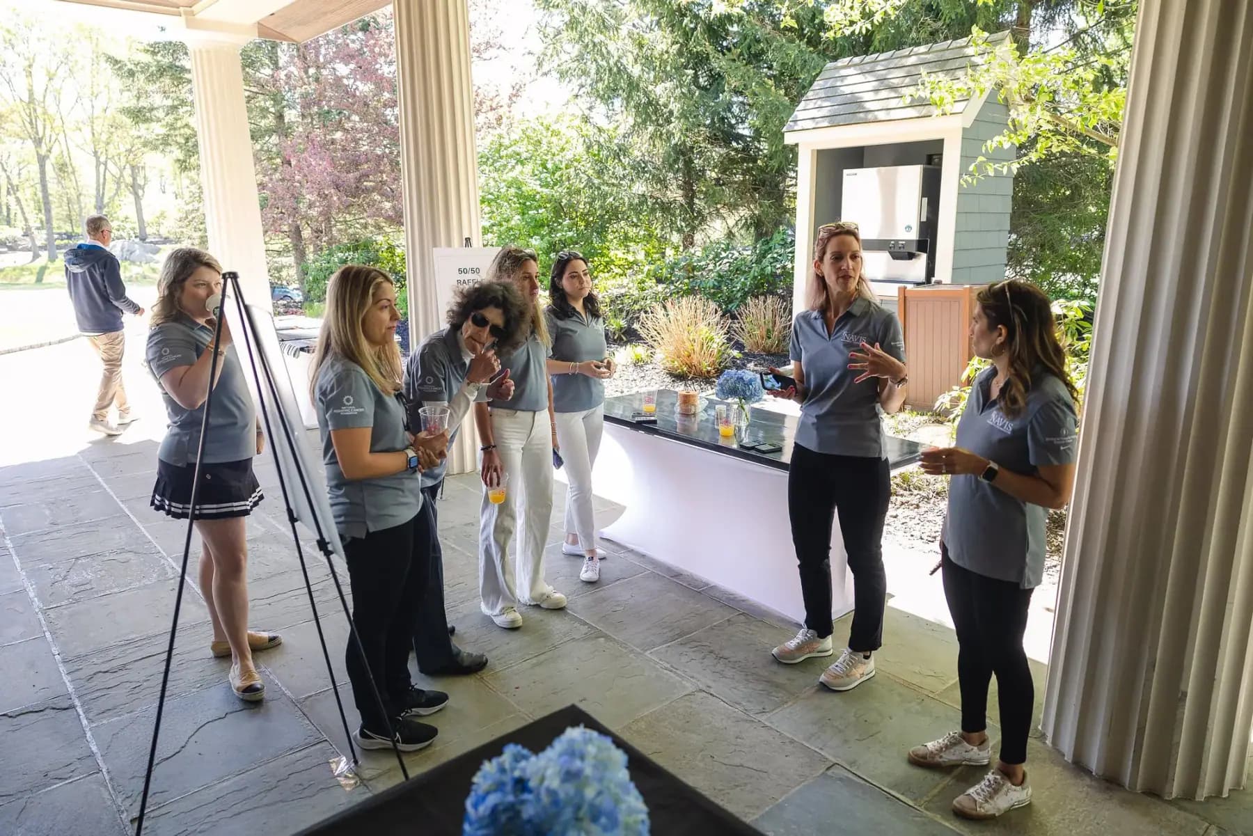 Volunteers in grey polos chatting at the registration area under the clubhouse portico