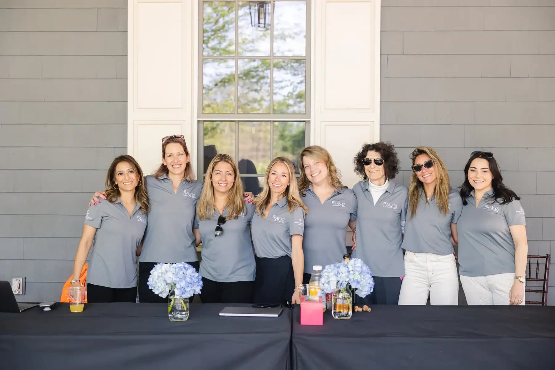 Eight volunteers in matching grey polos lined up behind a table decorated with hydrangeas