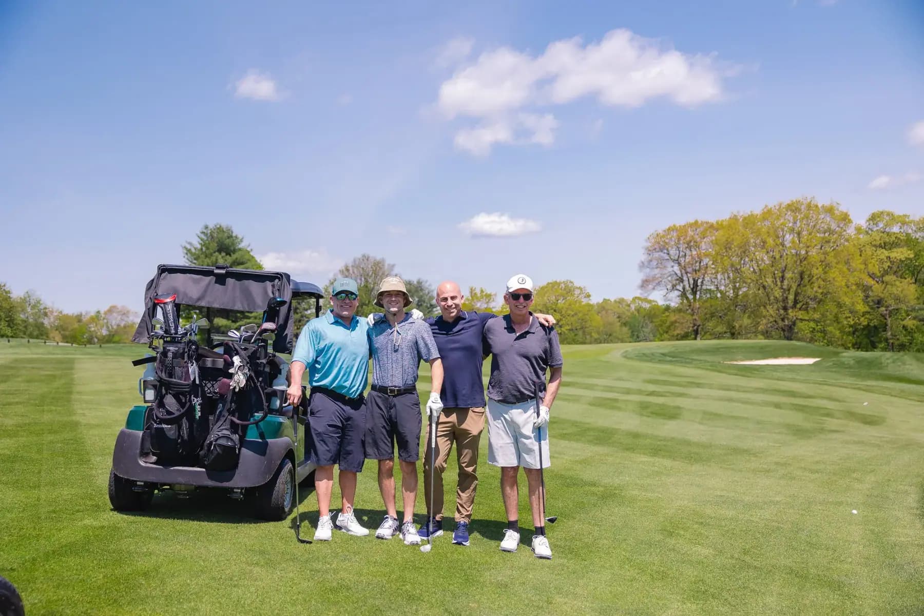 Foursome of golfers standing beside their cart on the course