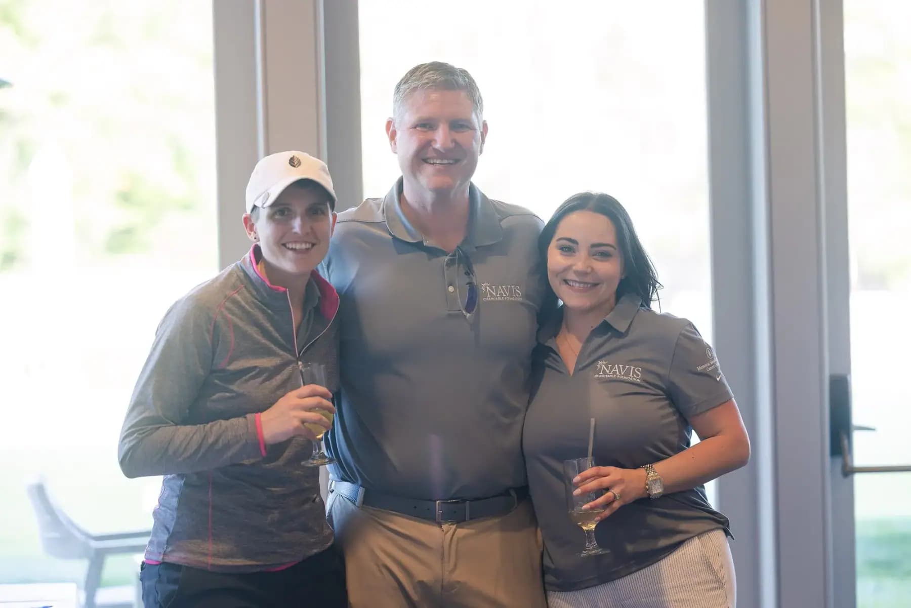 Man in a Navis polo posing indoors with two women holding drinks