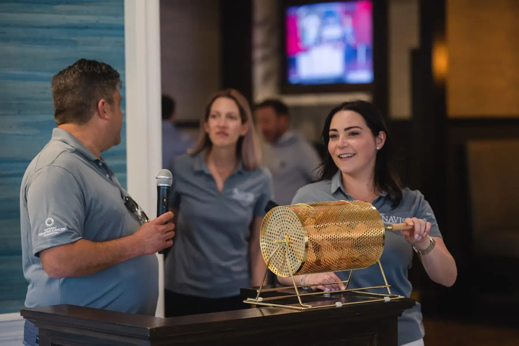 Volunteers drawing raffle tickets from a brass drum as a man speaks into a microphone