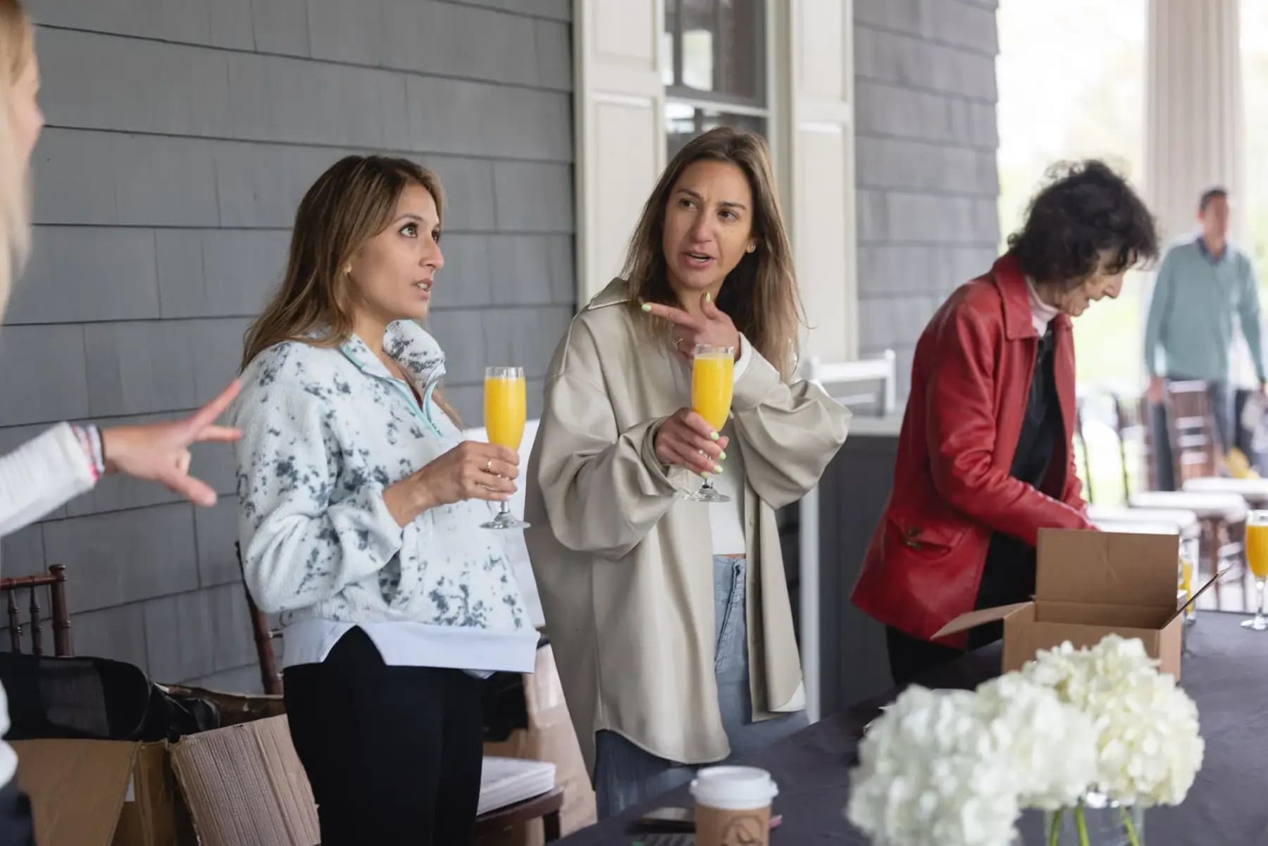 Women holding mimosas chatting at the check-in table on the porch