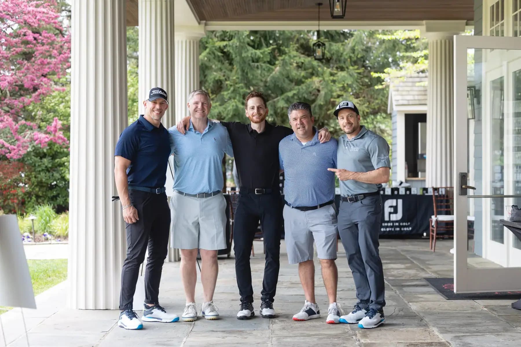 Five golfers posing under the clubhouse portico