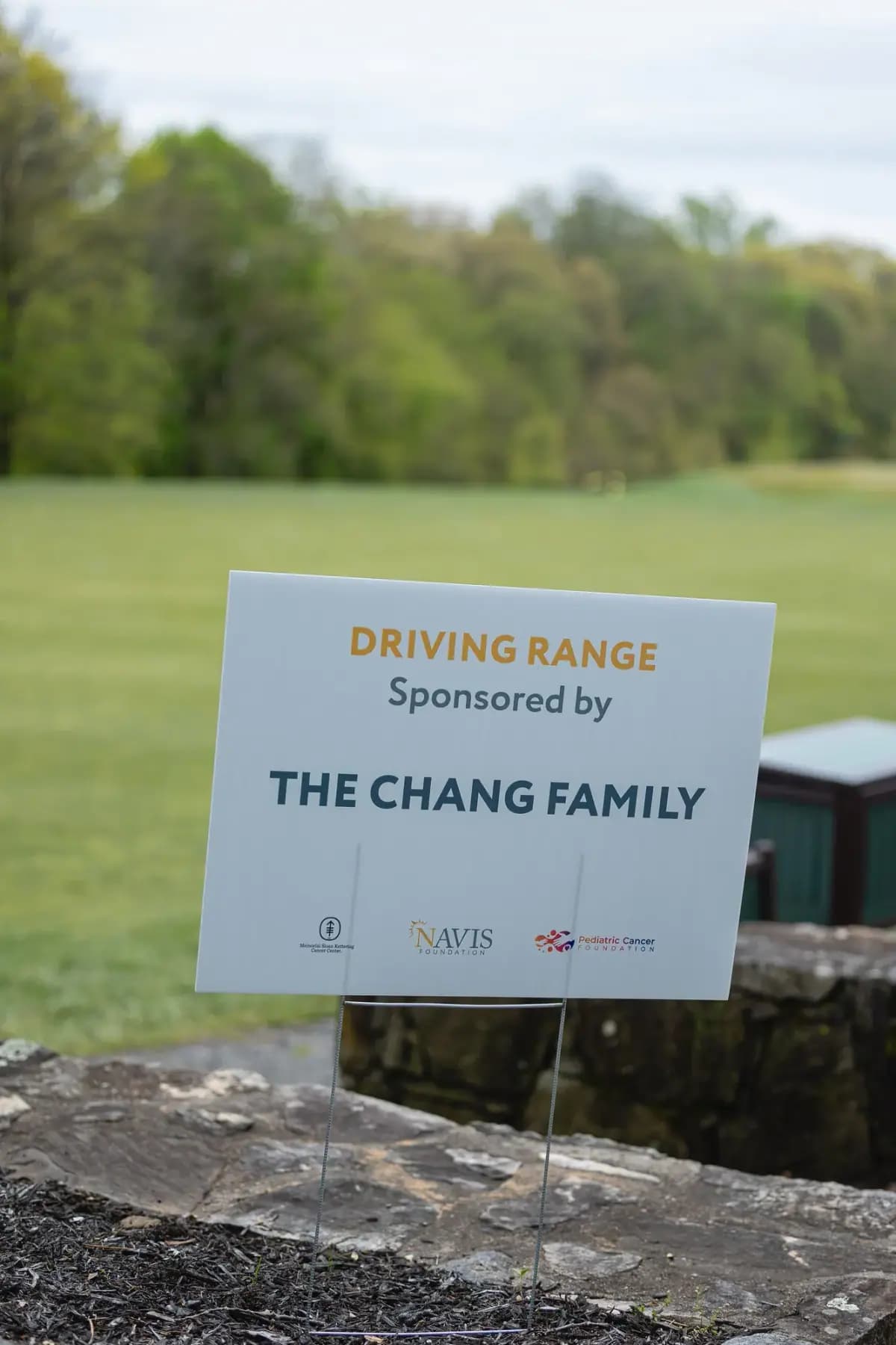 Driving range sign reading "Sponsored by The Chang Family" on a stone wall