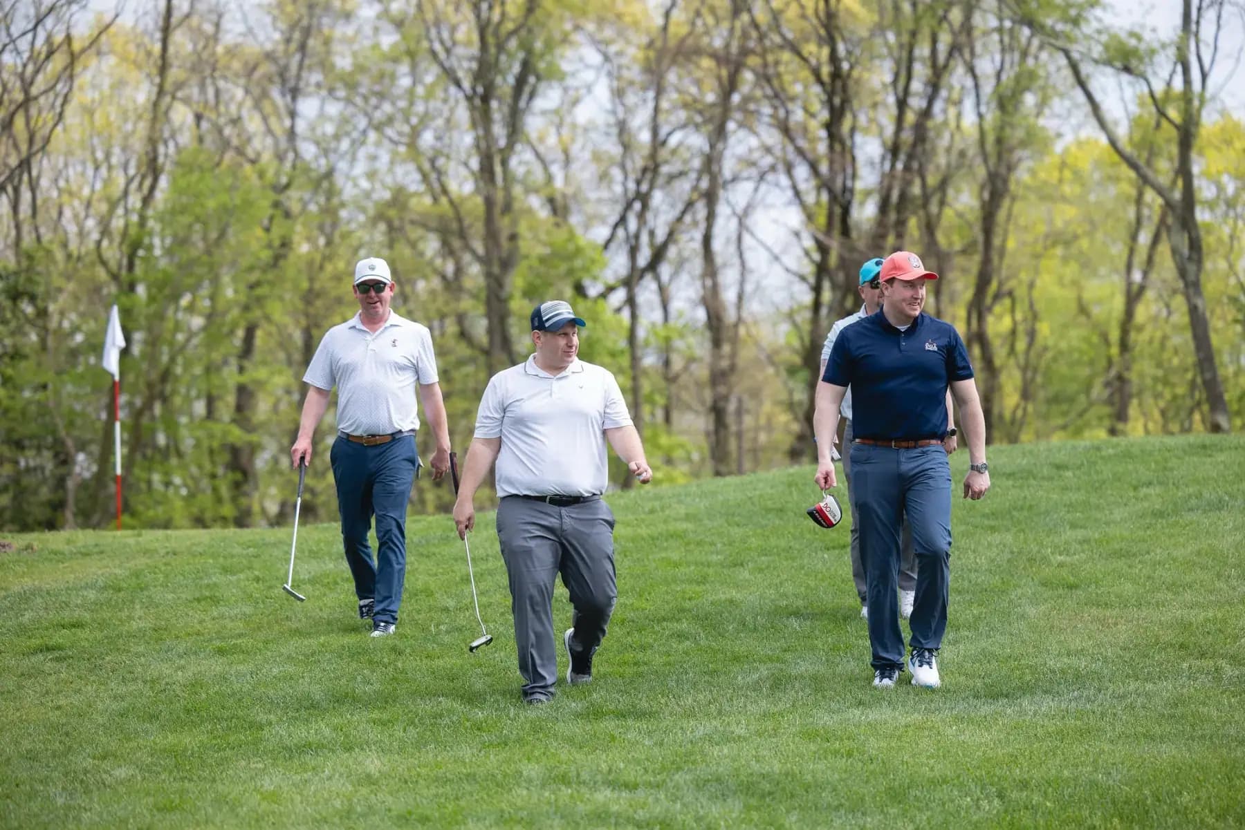 Three golfers walking up a grassy slope with clubs