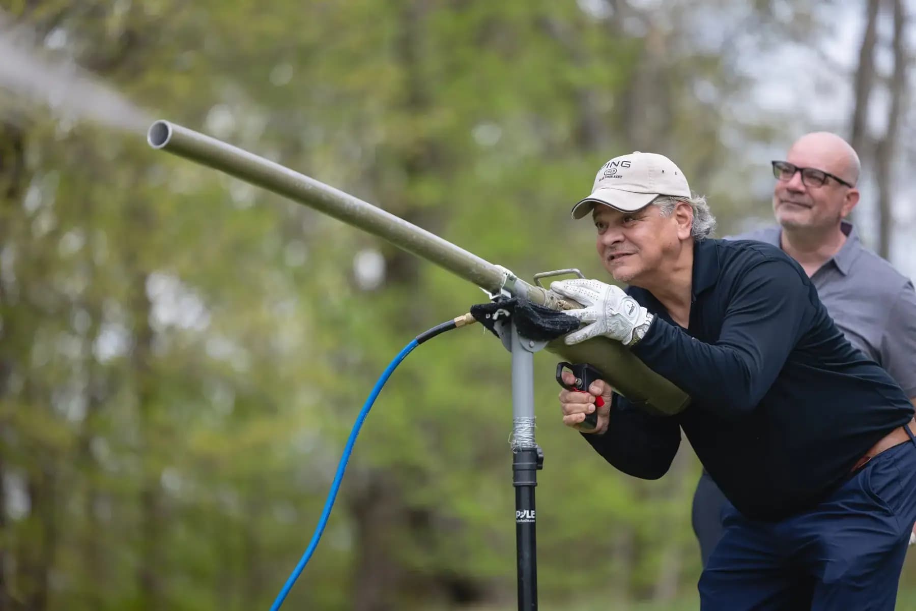 Golfer aiming a golf ball launcher cannon while another man watches