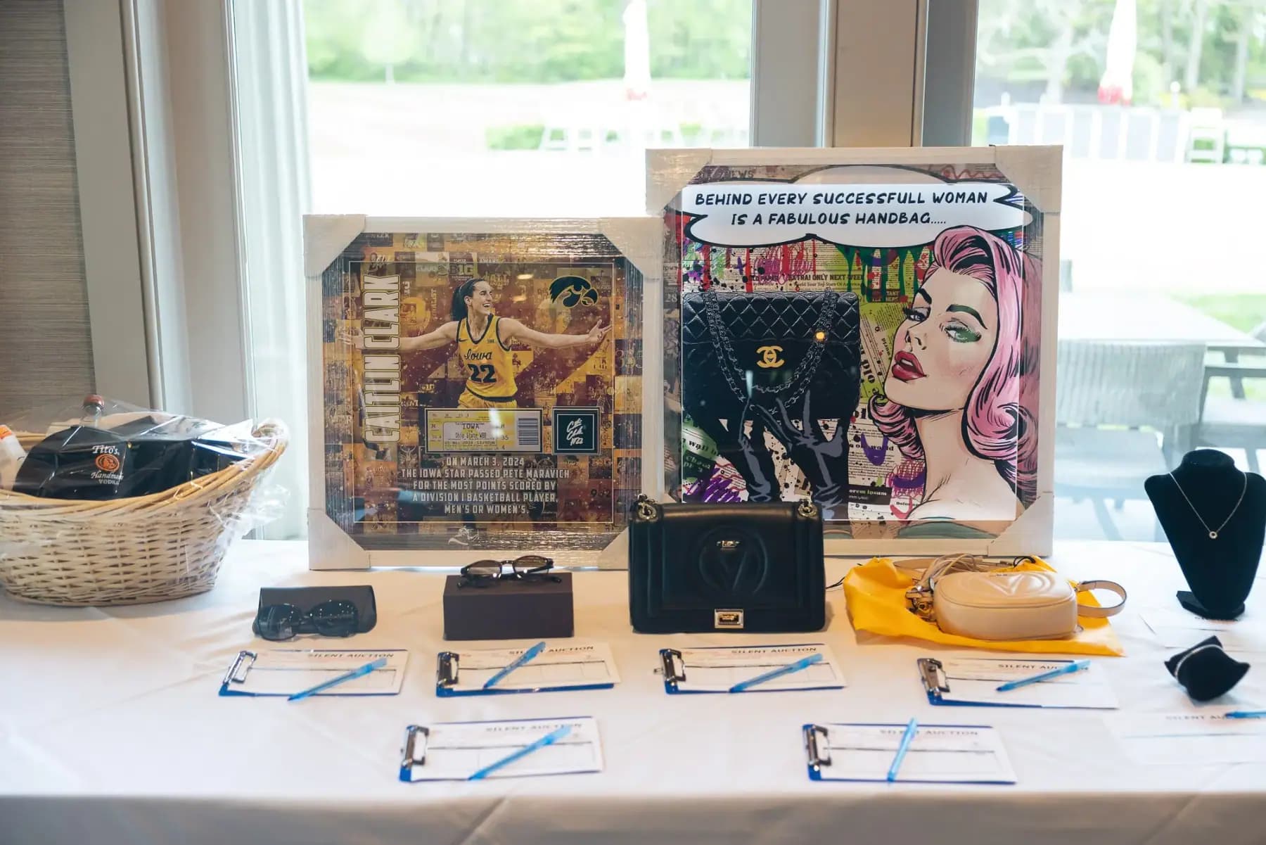 Silent auction table with framed pop art, handbags and bid sheets