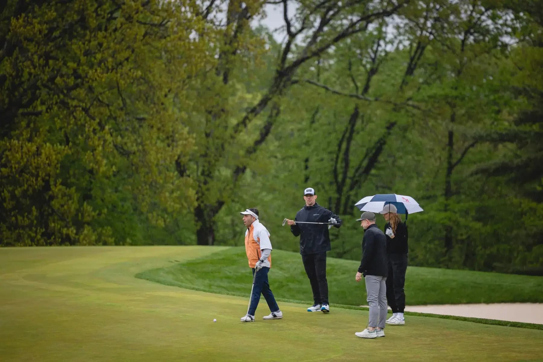 Golfers with umbrellas on an overcast green beside the cart path
