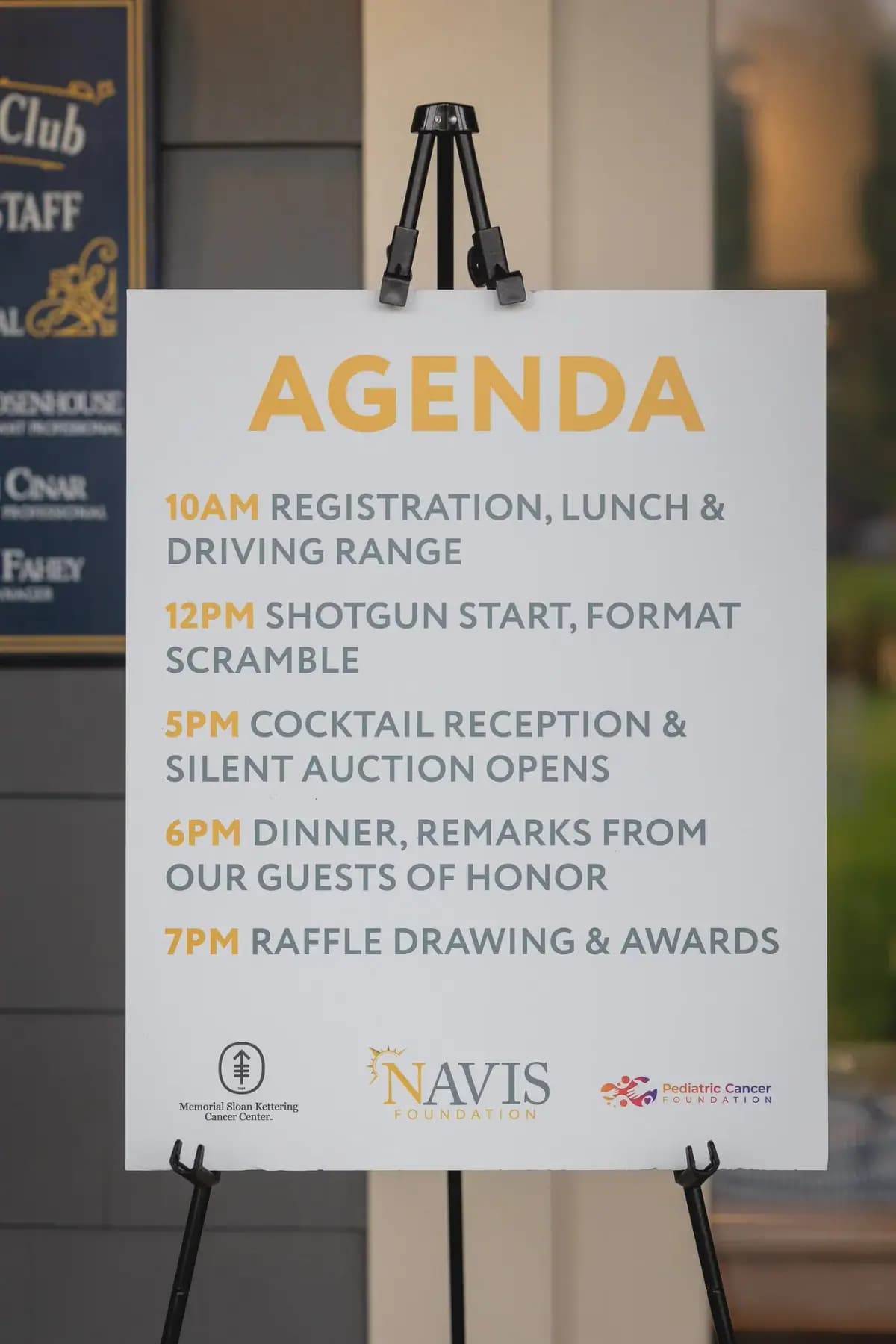Event agenda sign on an easel listing registration, shotgun start, cocktails, dinner and raffle times