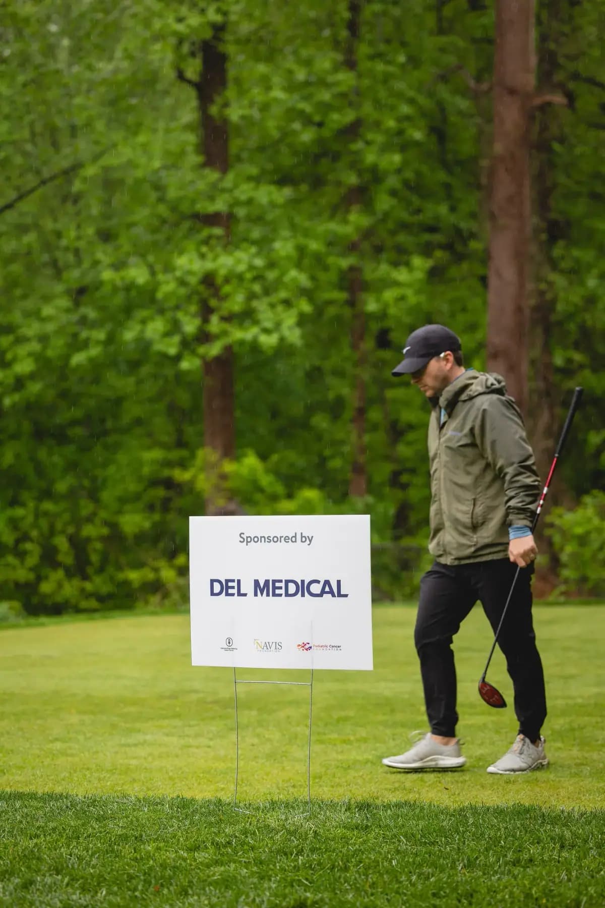 Golfer walking past a Del Medical hole sponsor sign