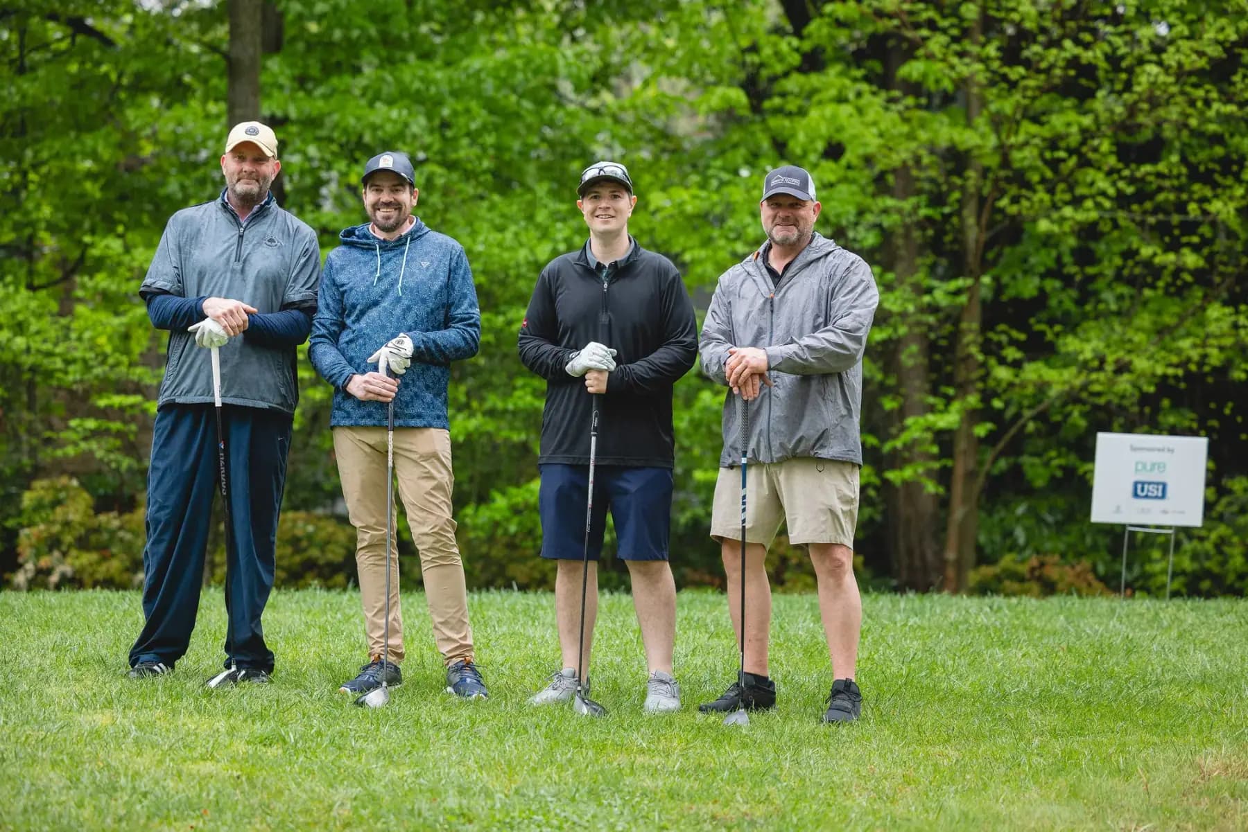 Four golfers in jackets posing on a fairway