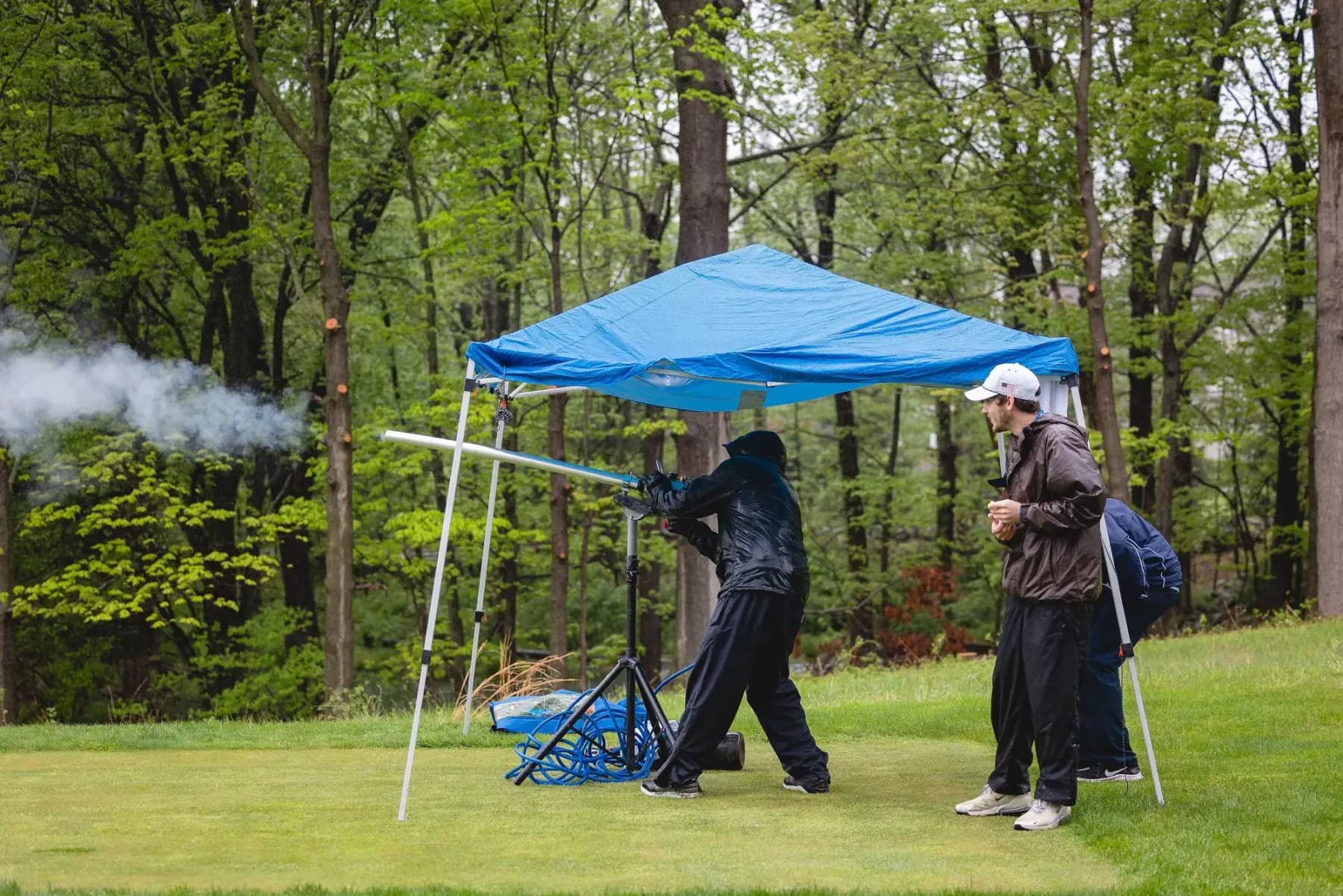 Golfer firing a golf ball launcher under a blue canopy as another watches