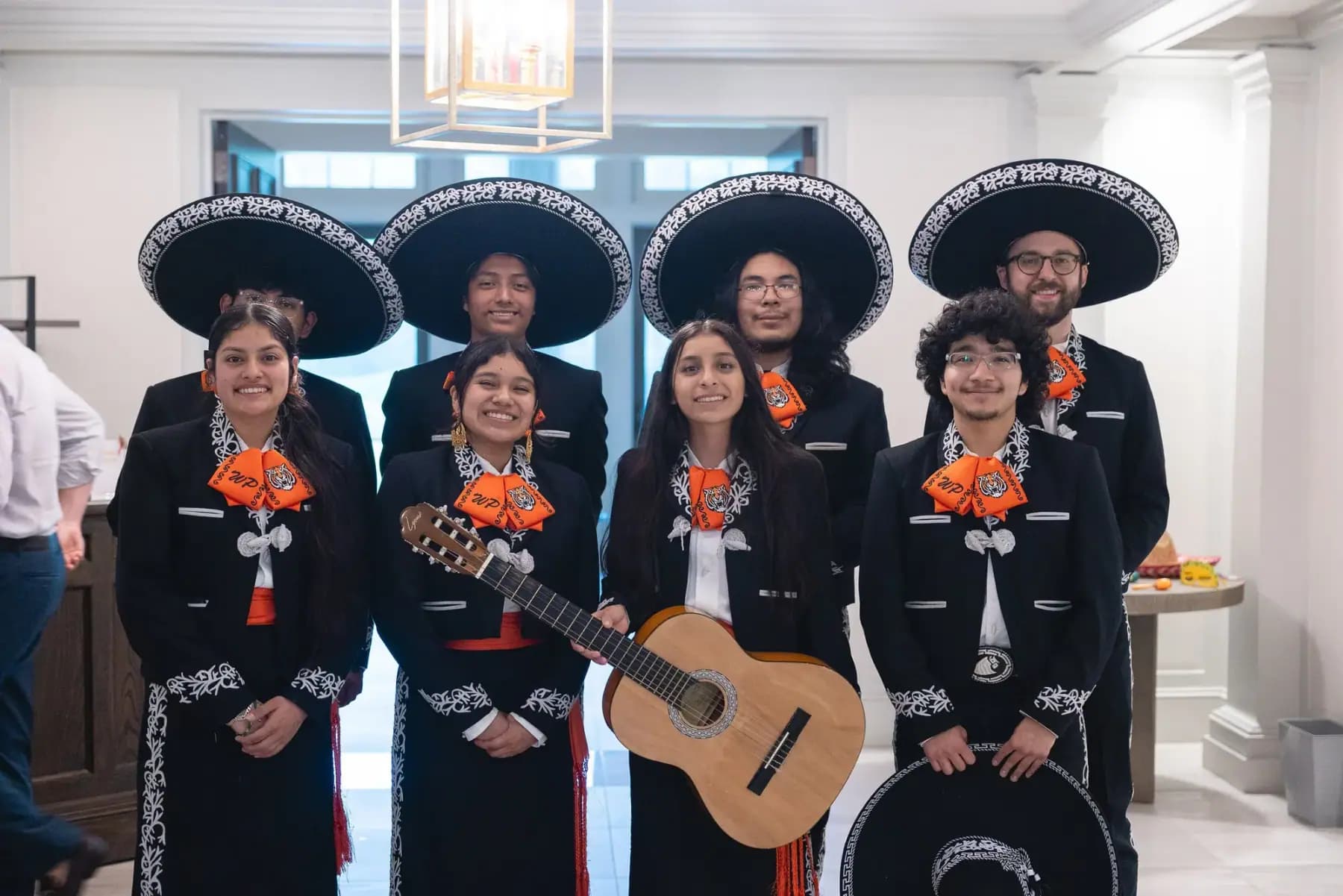 Mariachi band members posing together, one holding a guitar