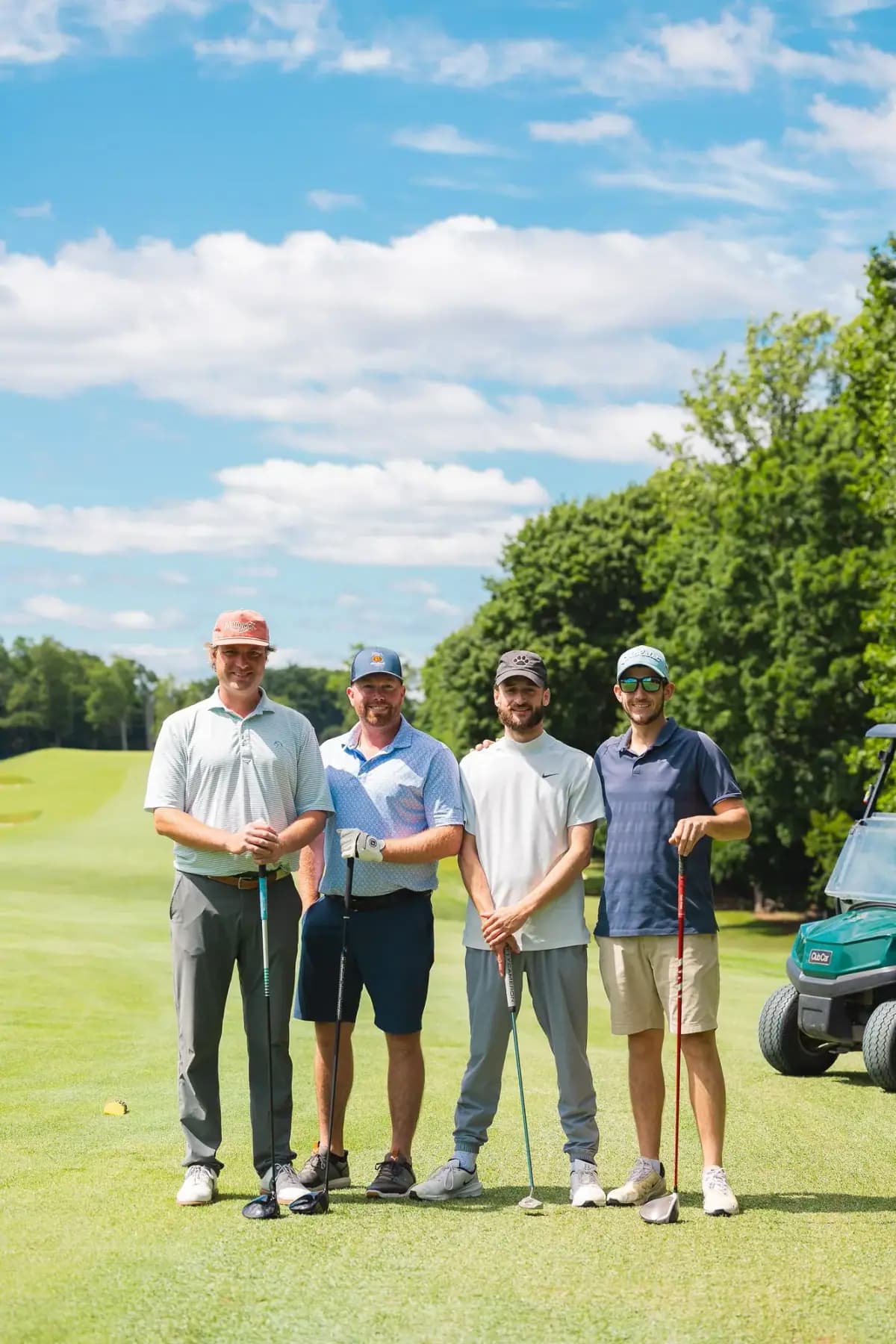 Four golfers posing on a fairway under a blue sky with a cart nearby