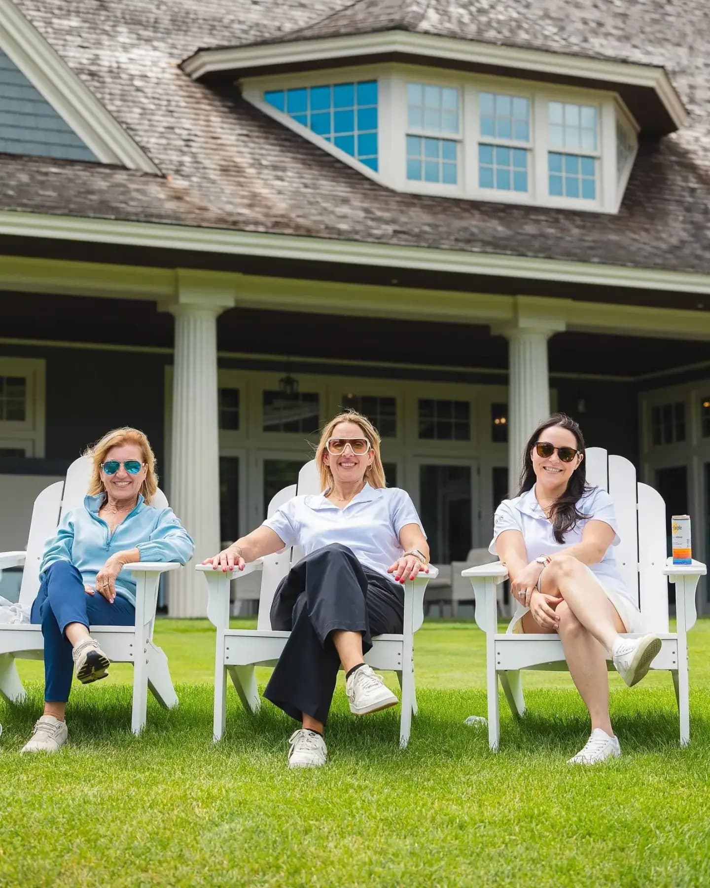 Three women relaxing in white Adirondack chairs in front of the clubhouse