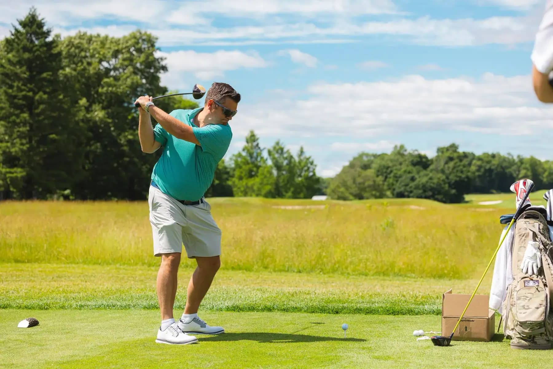 Golfer in a teal shirt mid-swing on a sunny tee box