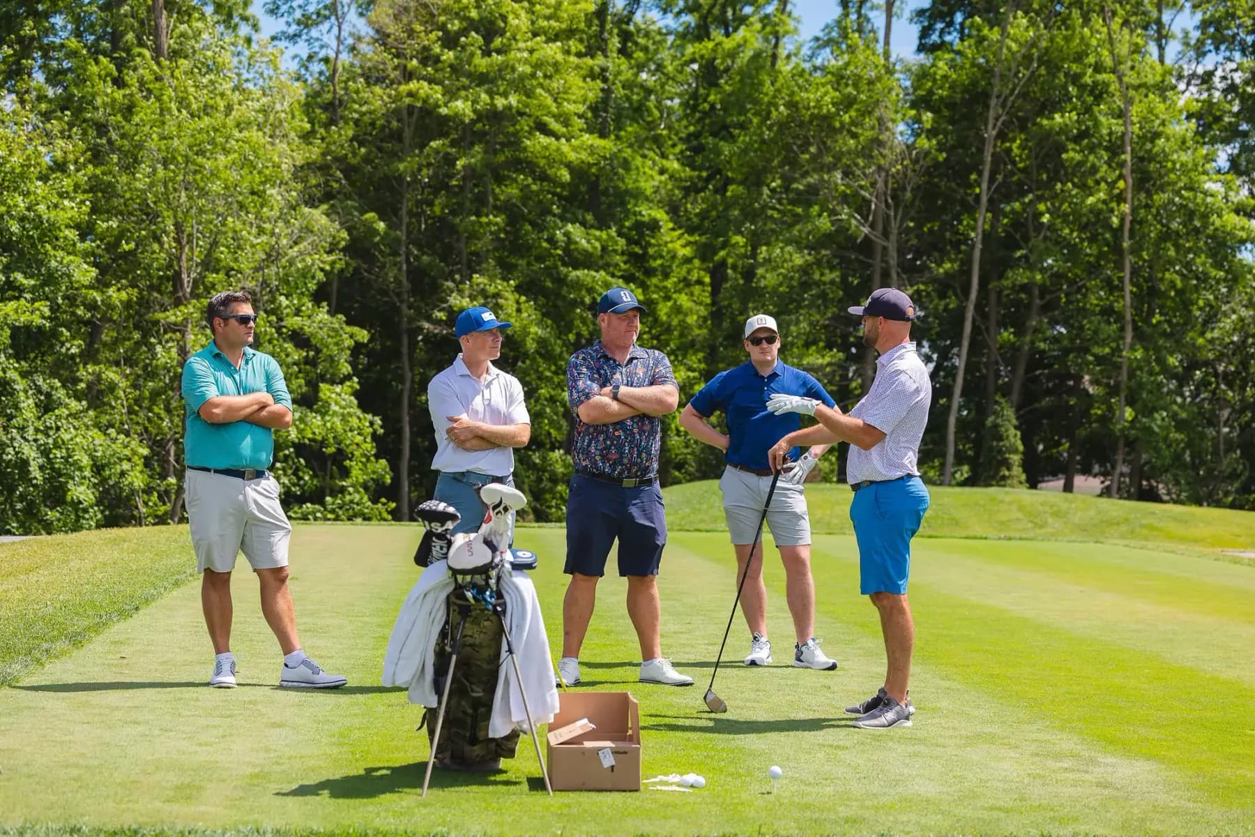 Five golfers standing around their bags on a tee box