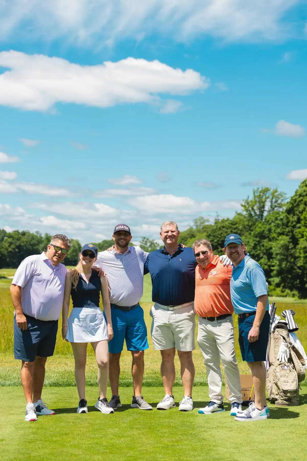 Six golfers posing on a tee box under blue sky