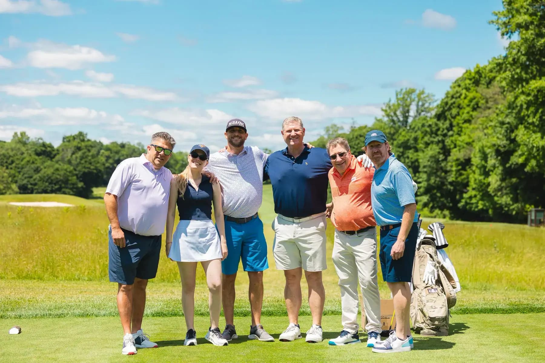 Six golfers posing on a tee box with bags beside them