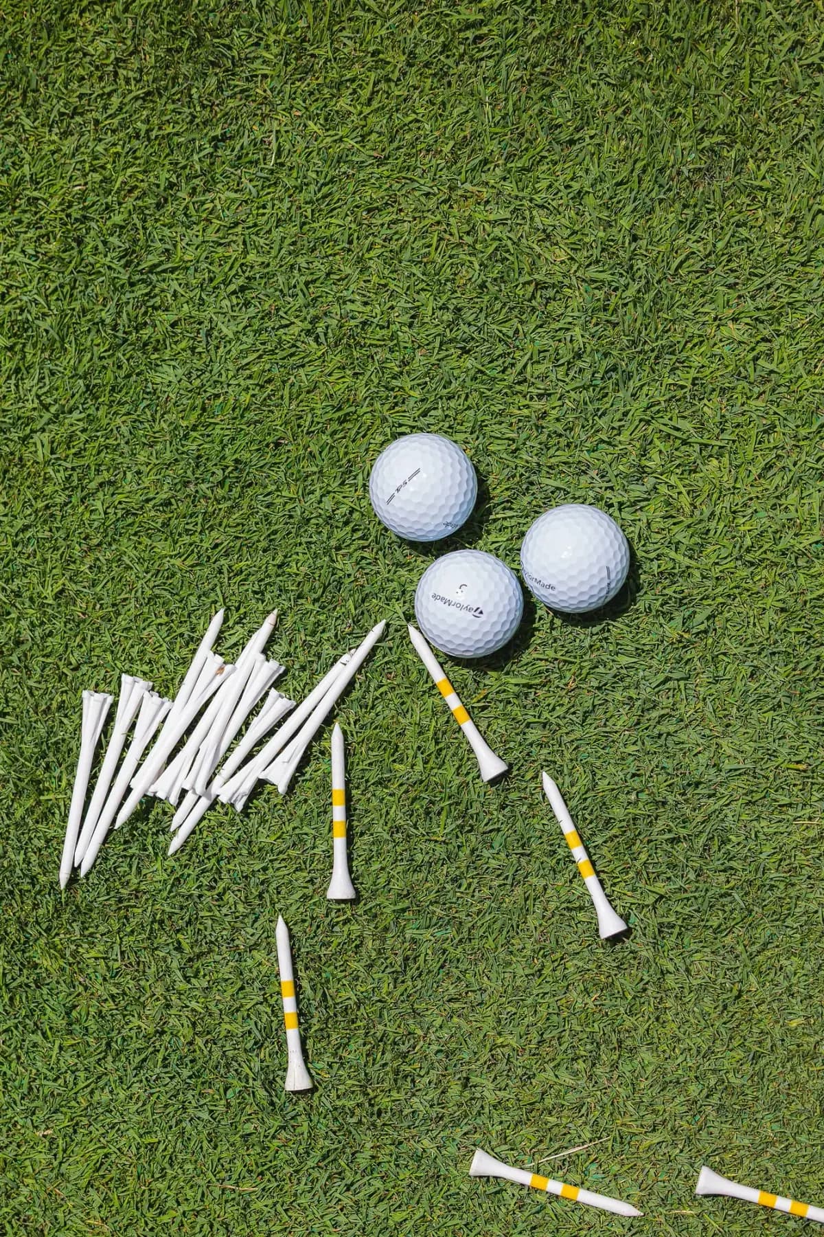 Golf balls and white tees scattered on grass, viewed from above