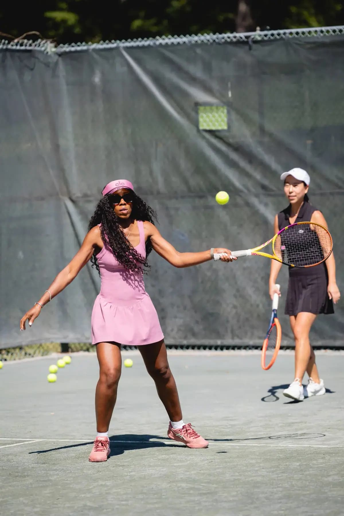Two women hitting balls on a court, one in a pink dress