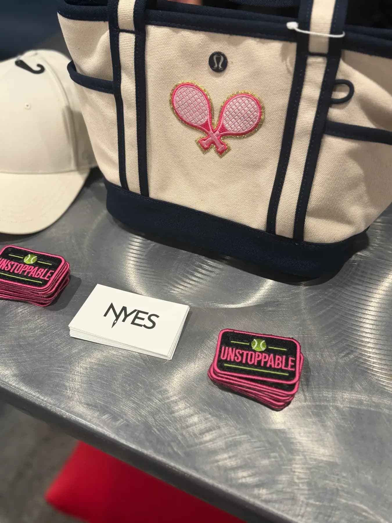 Tote bag with a racket patch beside UNSTOPPABLE patches and an NYES card